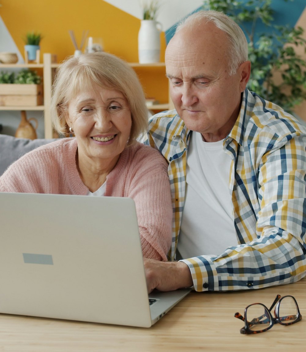 Un couple de retraités, souriant, devant un ordinateur portable chez lui