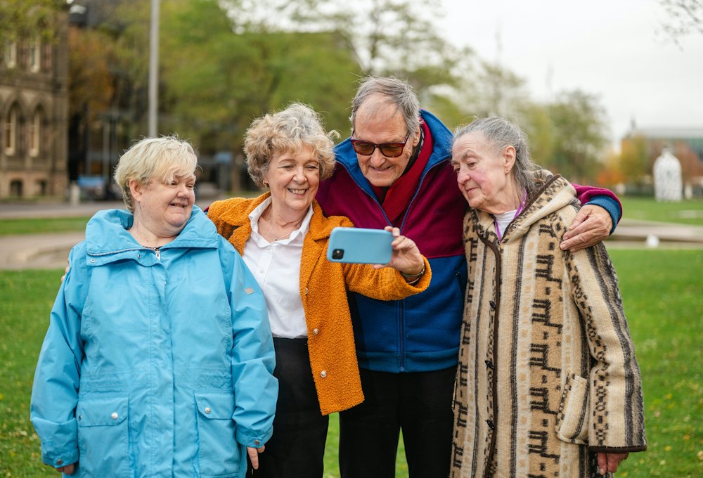 Quatre amis retraités, souriants, prennent un selfie avec un smartphone